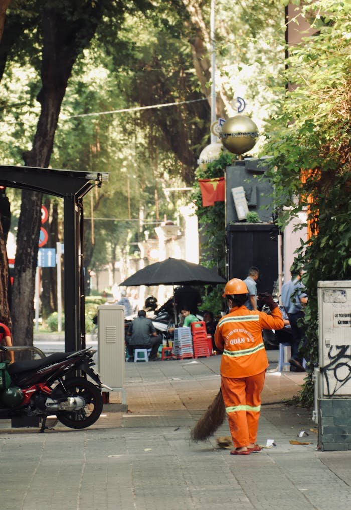 A man in orange clothing is sweeping the sidewalk